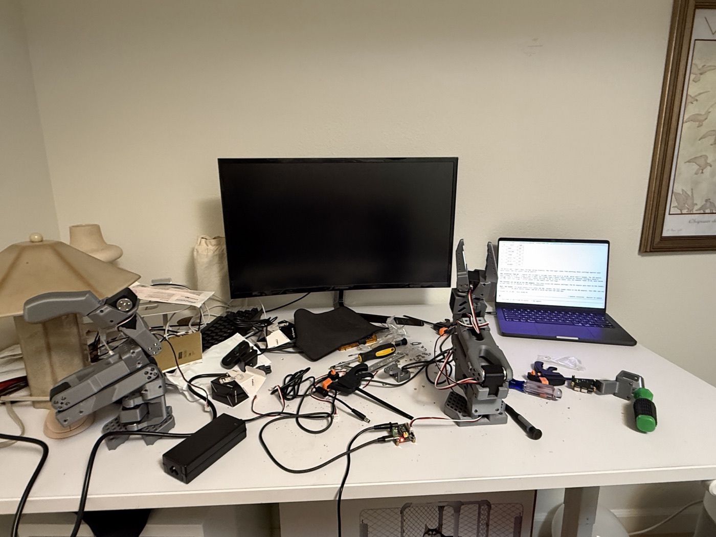 The workbench mid-build: leader arm on the left, follower arm on the right, controller board in front, tools and cables around them.